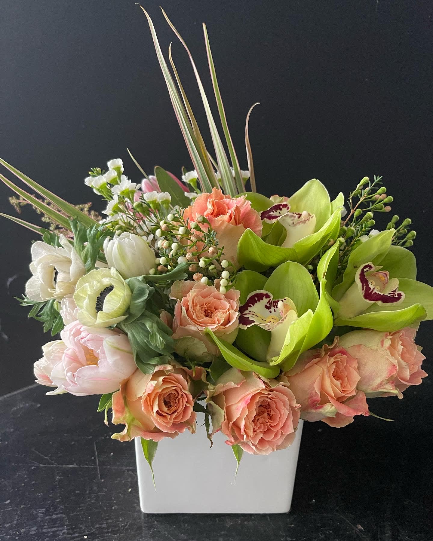 Mixed bouquet in a white square vase with peach roses and green orchids