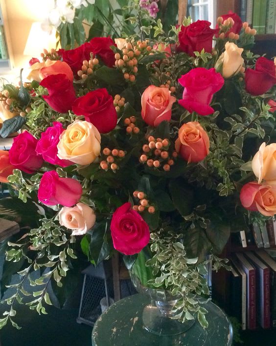 Large bouquet of red, pink, and peach roses with berries in a clear glass pedestal vase