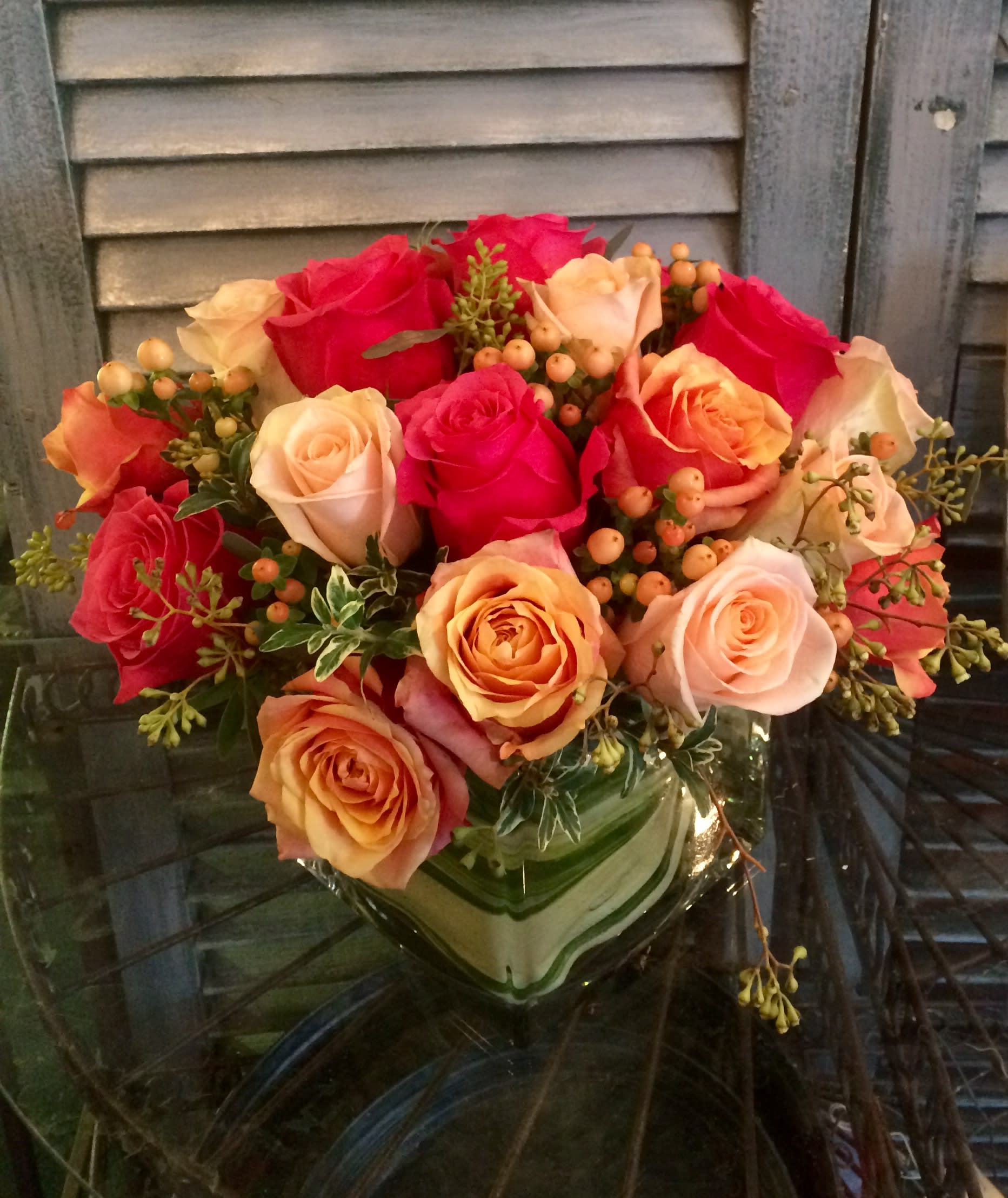 Compact arrangement of pink and peach roses with berries in a square glass vase