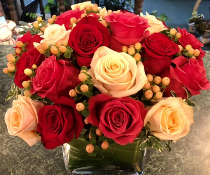 Compact arrangement of red and cream roses with peach berries in a clear glass cube vase