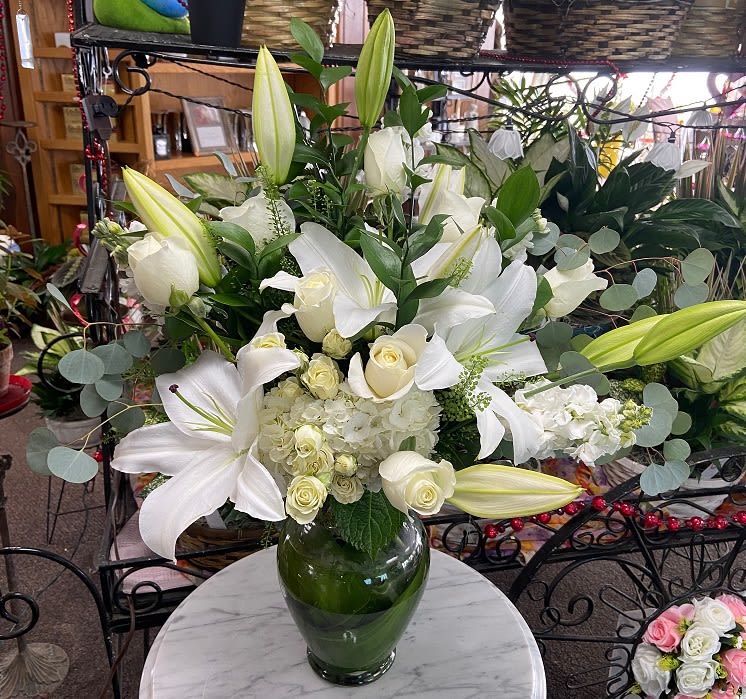 Tall arrangement of white lilies, roses, and hydrangeas in a clear glass vase