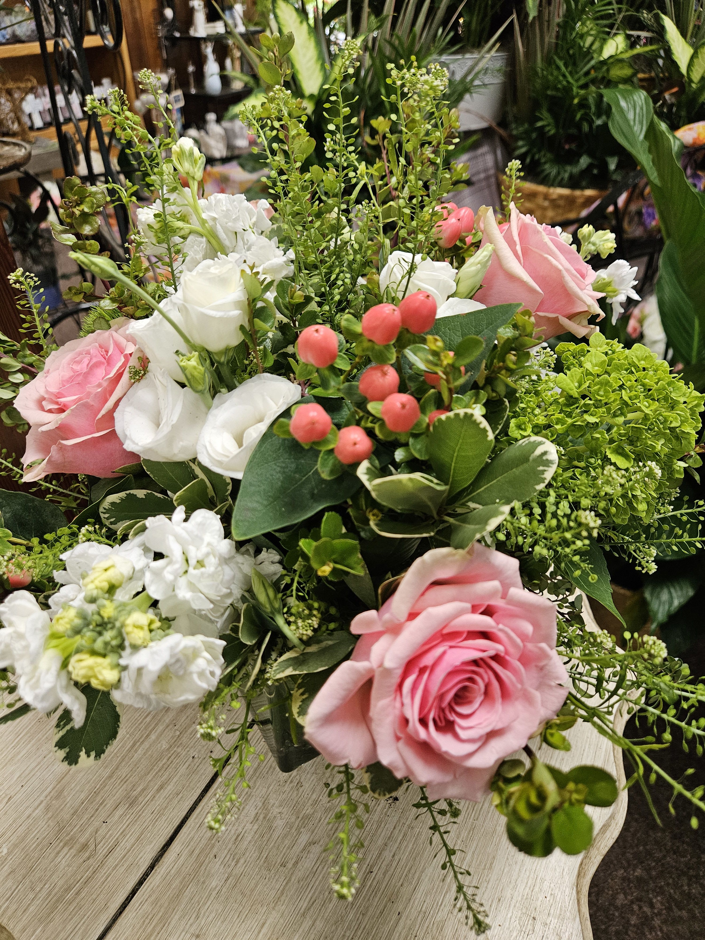 Pink roses and white blooms with berries in a lush mixed arrangement in a glass vase