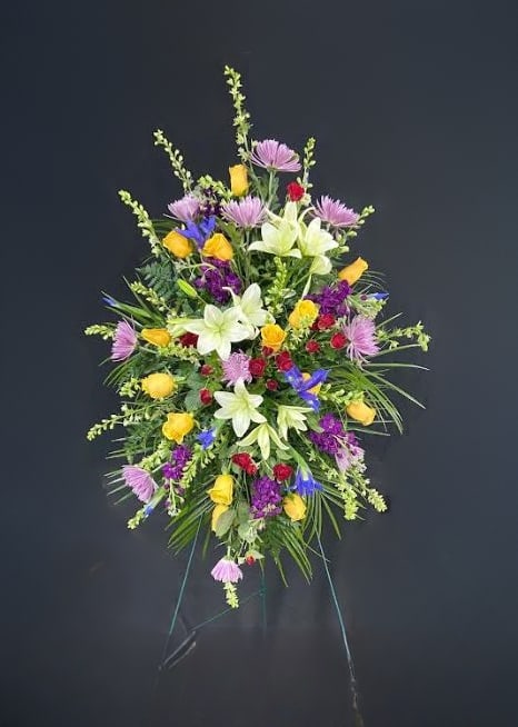 Tall standing spray with yellow roses, white lilies, and mixed purple flowers on an easel