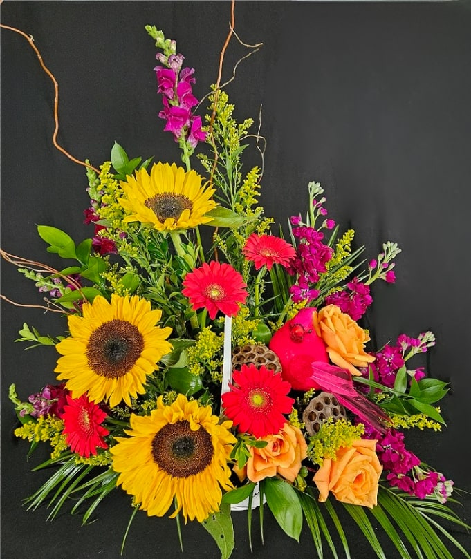 Colorful arrangement of sunflowers, orange roses, and hot pink gerbera daisies in a low white container.