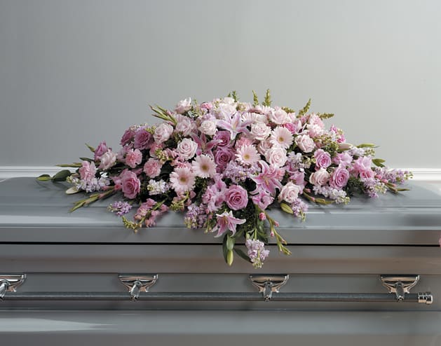 Pink and lavender casket spray with roses, lilies, and other blooms on a gray casket