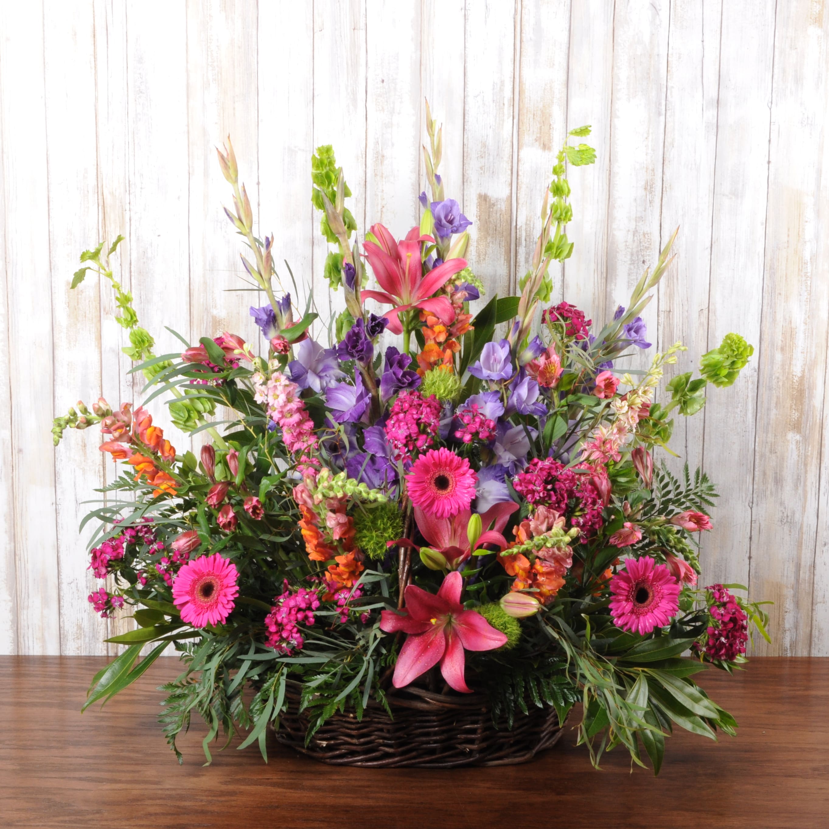 Tall mixed arrangement of pink lilies, gerbera daisies, and assorted blooms in a wicker basket