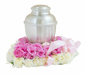 Pink roses arranged around a silver urn with a pink ribbon