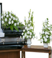 White floral funeral arrangements in white vases beside a casket