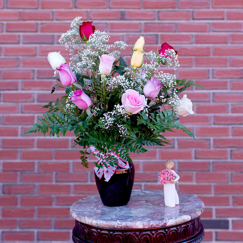 Mixed pink and white roses in a dark vase with a small figurine beside it
