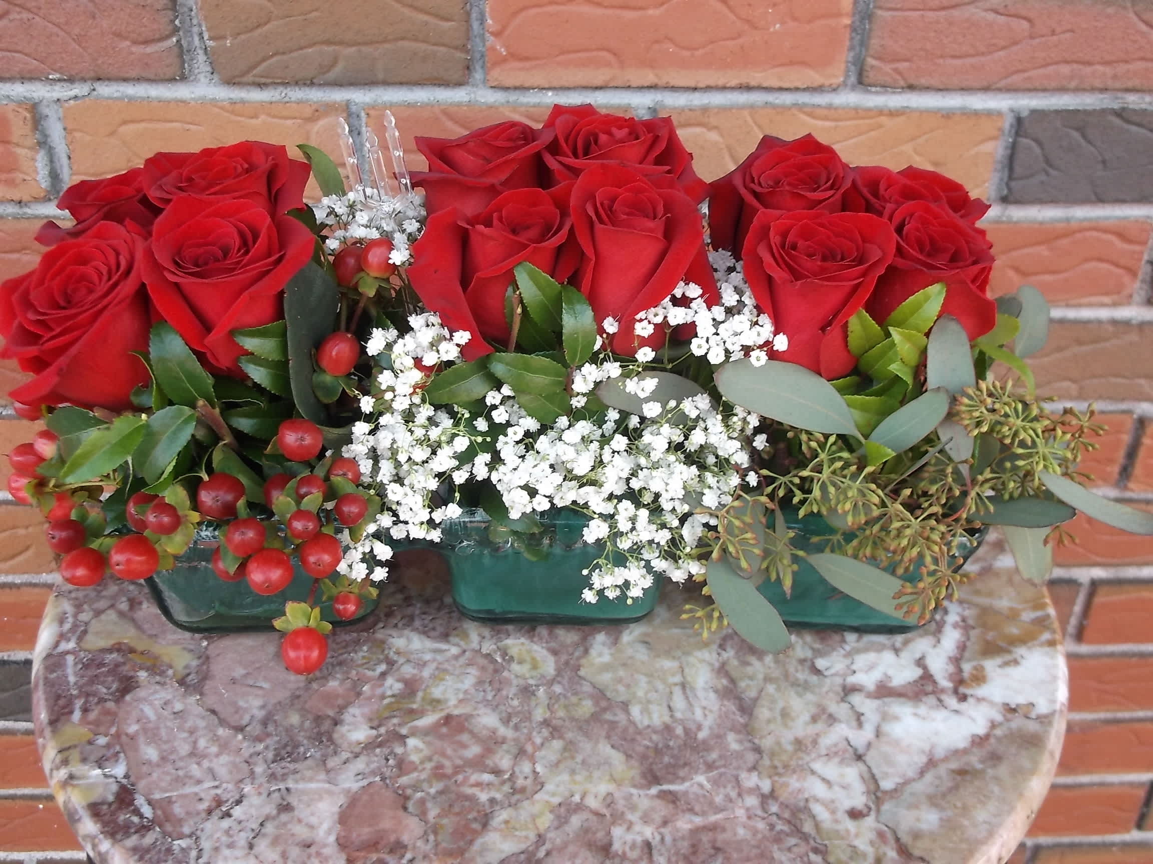 Red roses arranged in three small glass containers with white filler flowers