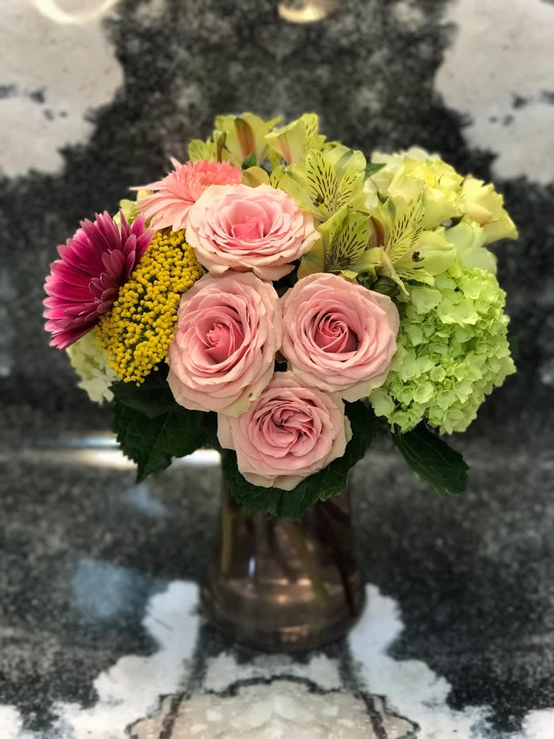 Mixed bouquet of pink roses, hydrangea, and yellow flowers in a vase