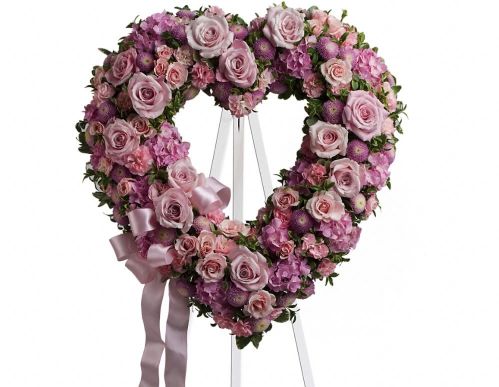 Heart-shaped pink floral wreath on a stand with a ribbon bow