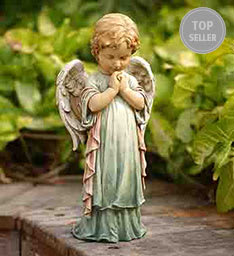 Small praying angel figurine in a garden setting