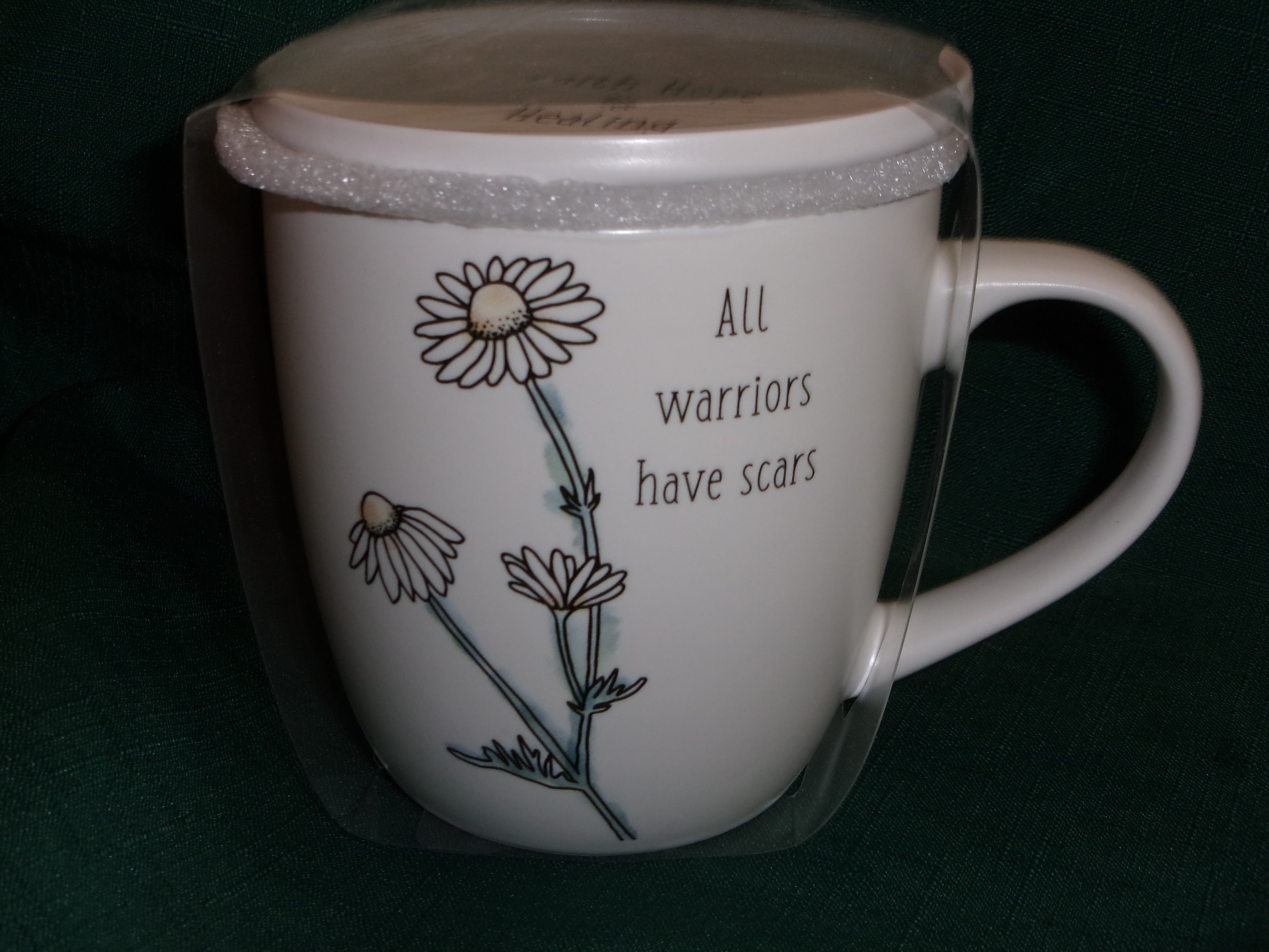 White mug with daisy illustration and the words "All warriors have scars"