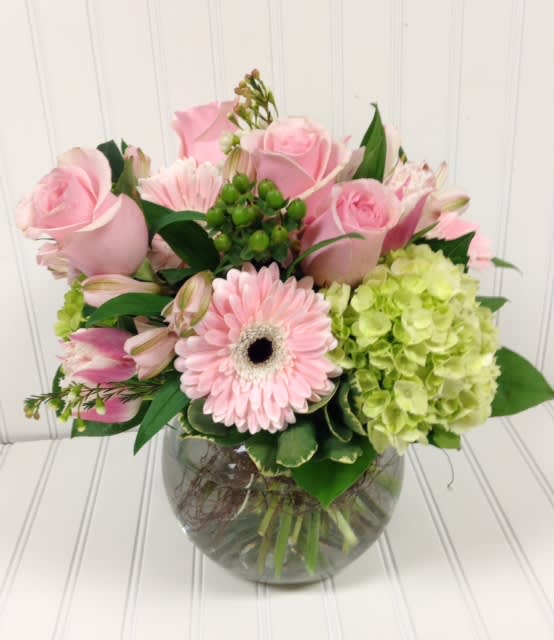 Pink roses and a gerbera daisy in a glass vase with green hydrangea