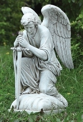 Stone angel statue kneeling in grass with folded wings