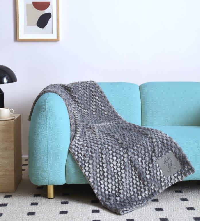 Gray knitted blanket draped over a light blue sofa in a living room
