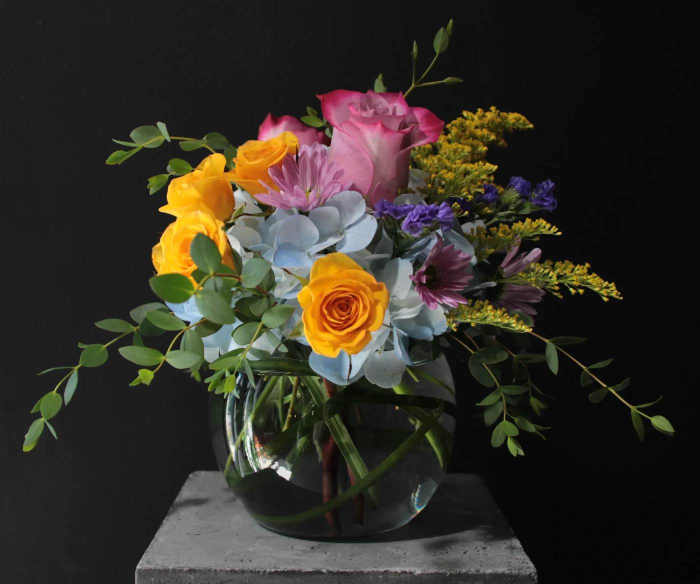 Mixed bouquet of roses, hydrangea, and purple flowers in a glass vase