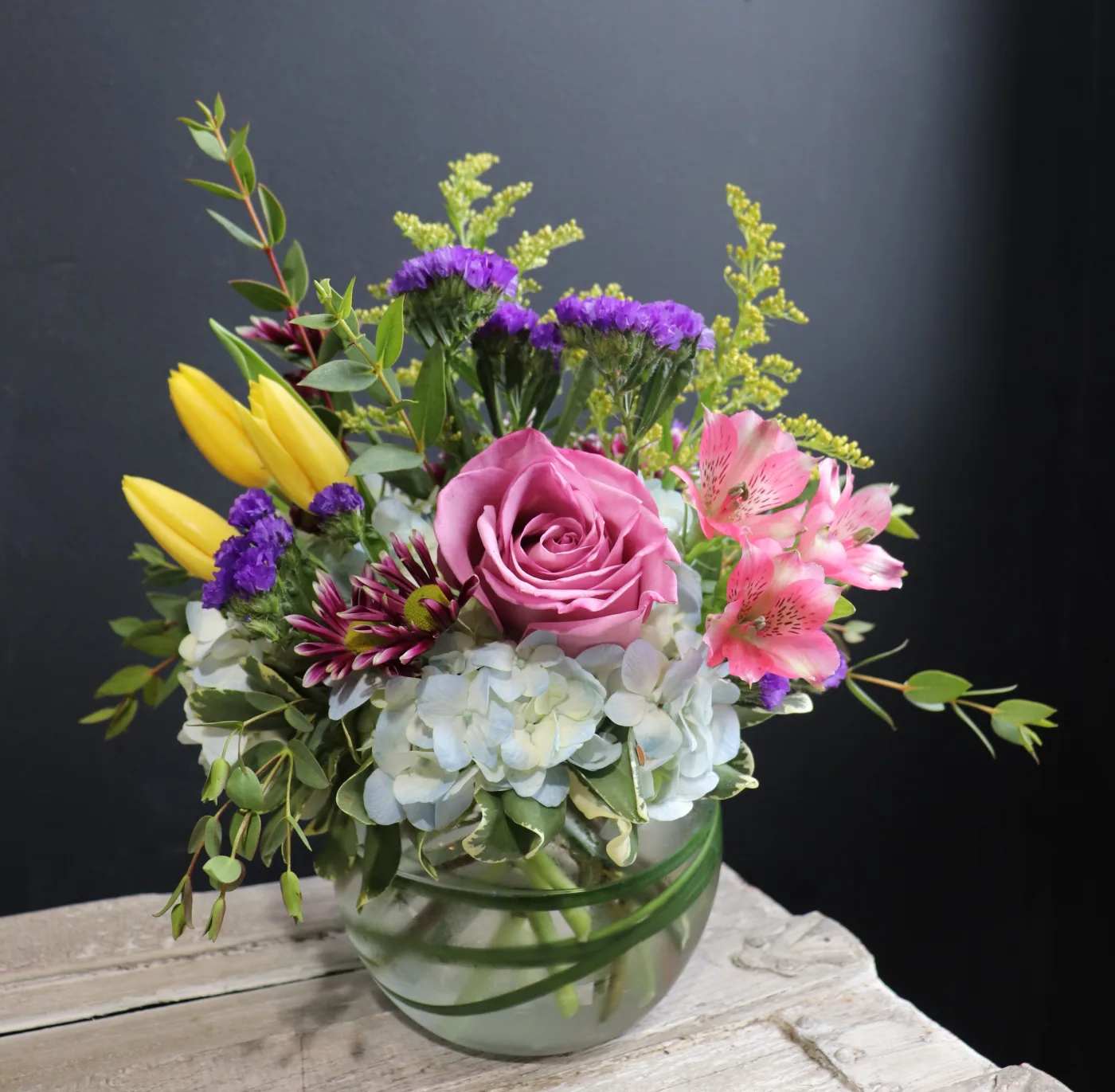 Mixed bouquet in a glass vase with a pink rose, yellow tulips, and pink alstroemeria
