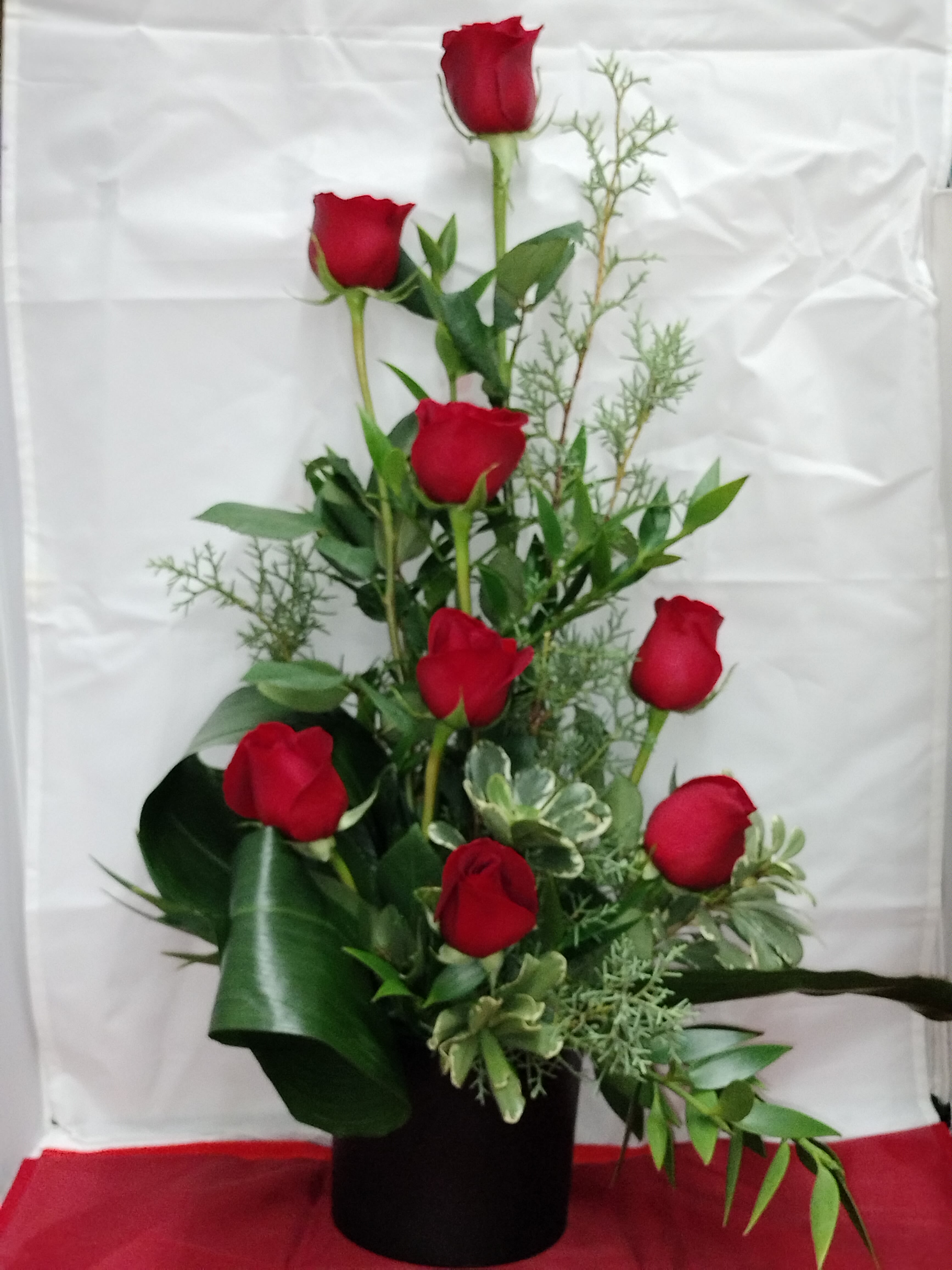 Tall arrangement of red roses in a black vase with greenery