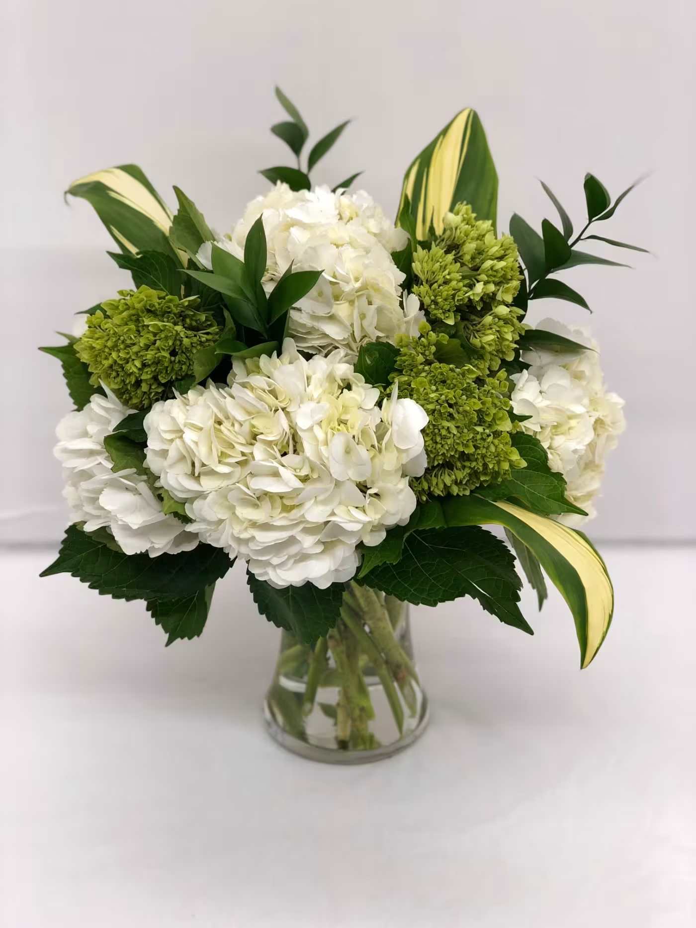 White hydrangea bouquet with green blooms in a clear glass vase