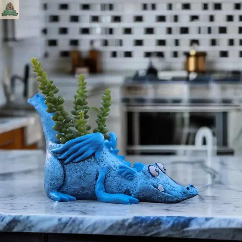 Lucky Blue Dragon Planter by Gisele Kratzner by Blob House with Tillandsia Air Plant or Succulent - Meet Lucky the Blue Dragon Blob House Planter, a charming, handcrafted poly-resin planter that guards your greenery with a playful grin. Part of the Blob House Designs Collection by Portland artist Gesine Krätzner, Lucky injects whimsy into any space. This compact dragon is ideal for succulents, air plants, or tiny herbs, whether perched on a shelf, windowsill, or patio.  Why Lucky stands out: its durable poly-resin build, lightweight feel, and weather-friendly design let you enjoy year-round color indoors or out. The vivid blue finish and silhouette instantly elevates décor, while practical features include good drainage and air circulation to support healthy roots.  Handcrafted poly-resin construction  Compact footprint for desks, shelves, and windowsills Lightweight and weather-resistant for indoor or outdoor use Ideal for succulents, air plants, and herbs; a delightful gift From a sunny windowsill to a cozy desk nook, Lucky adapts to a range of spaces and plant choices. It’s a thoughtful pick for plant lovers and fantasy fans seeking a unique, durable accent that sparks conversation and imagination.  Bring Lucky home today and let a touch of magic take root.   