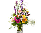 Tall mixed bouquet in a clear glass vase with purple, pink, and yellow flowers