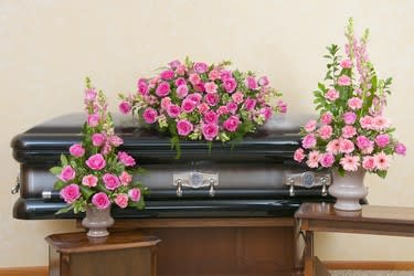 Pink floral arrangements displayed around a black casket