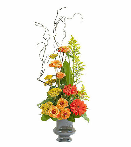 Orange roses and gerbera daisies in a gray vase with tall curly branches