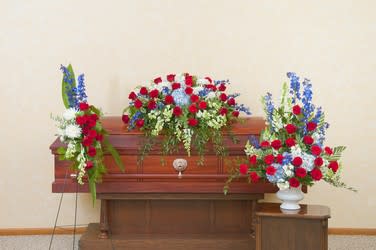 Three red, white, and blue floral sprays arranged around a wooden casket