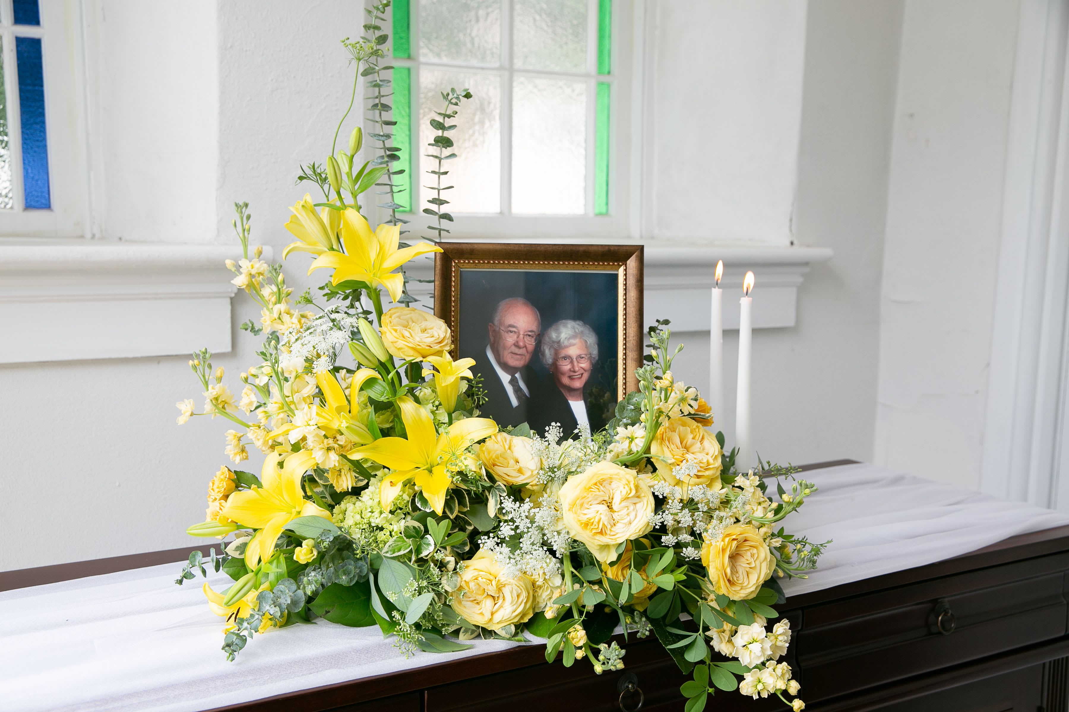 Yellow floral arrangement beside a framed photo and candles on a casket