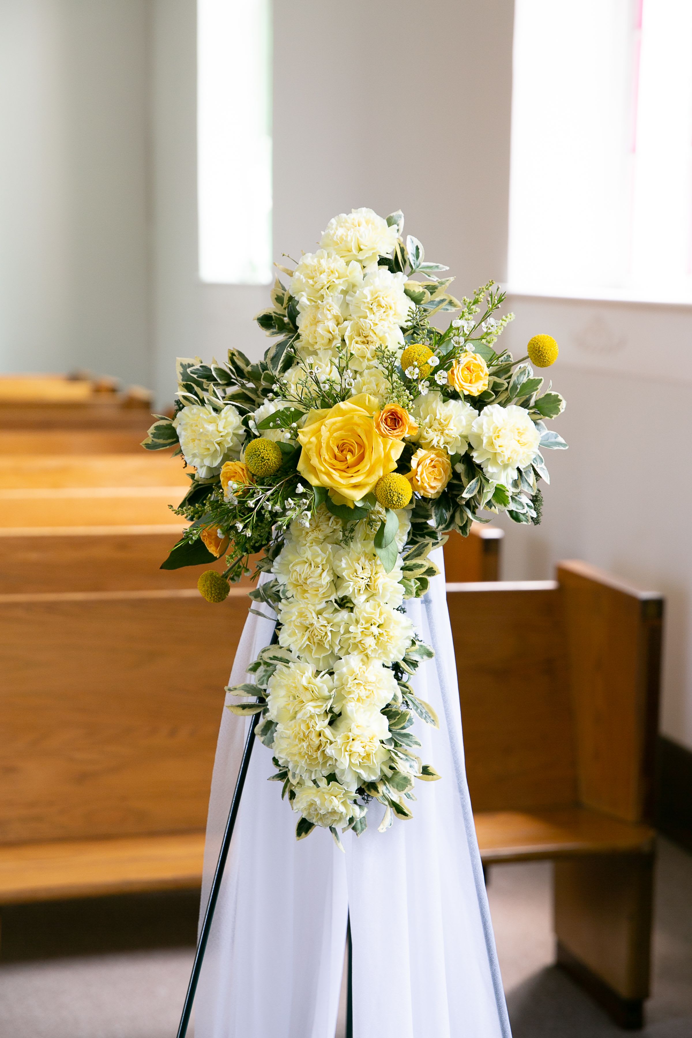 Yellow and white floral cross on a white stand in a church