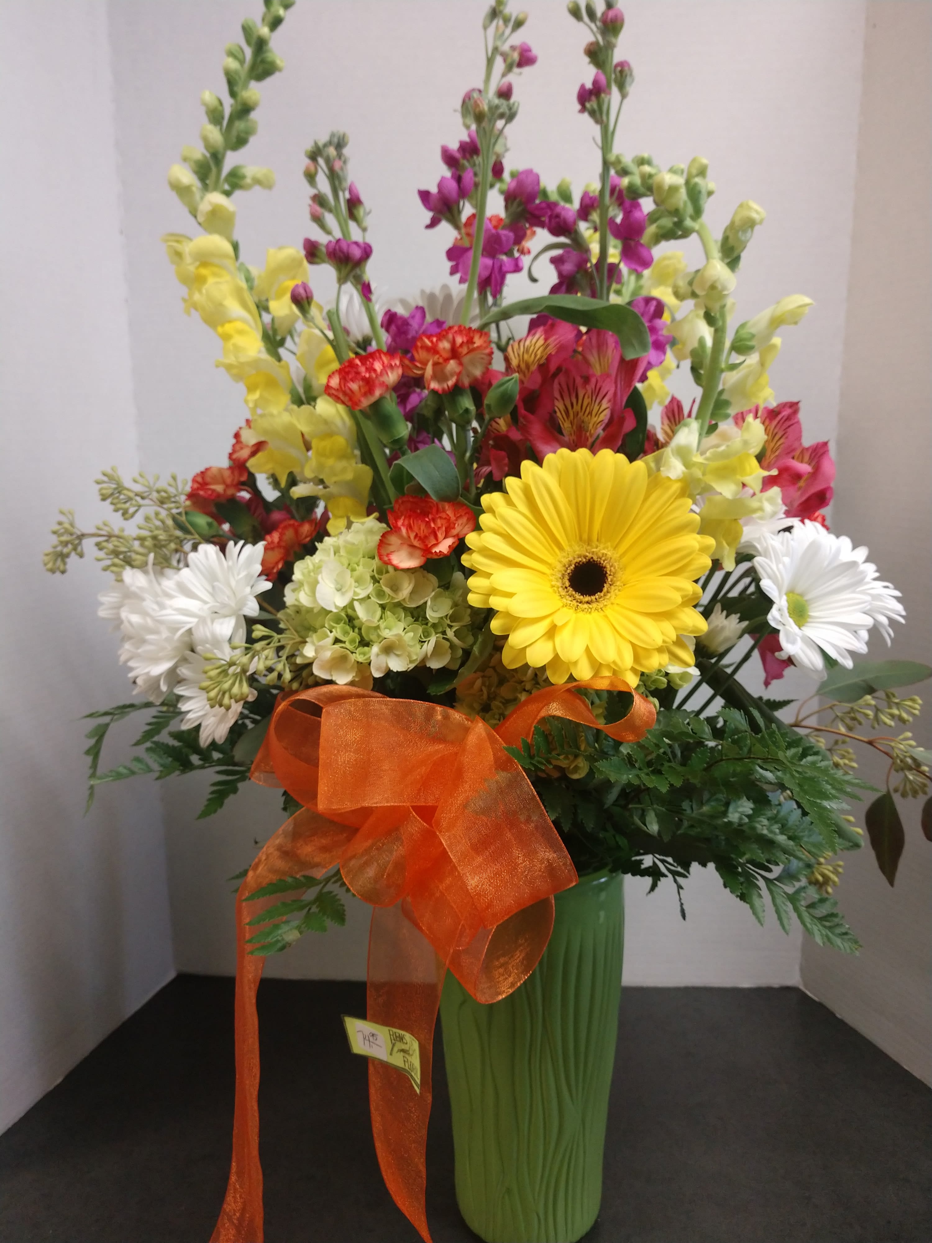 Mixed bouquet in a green vase with a large orange ribbon