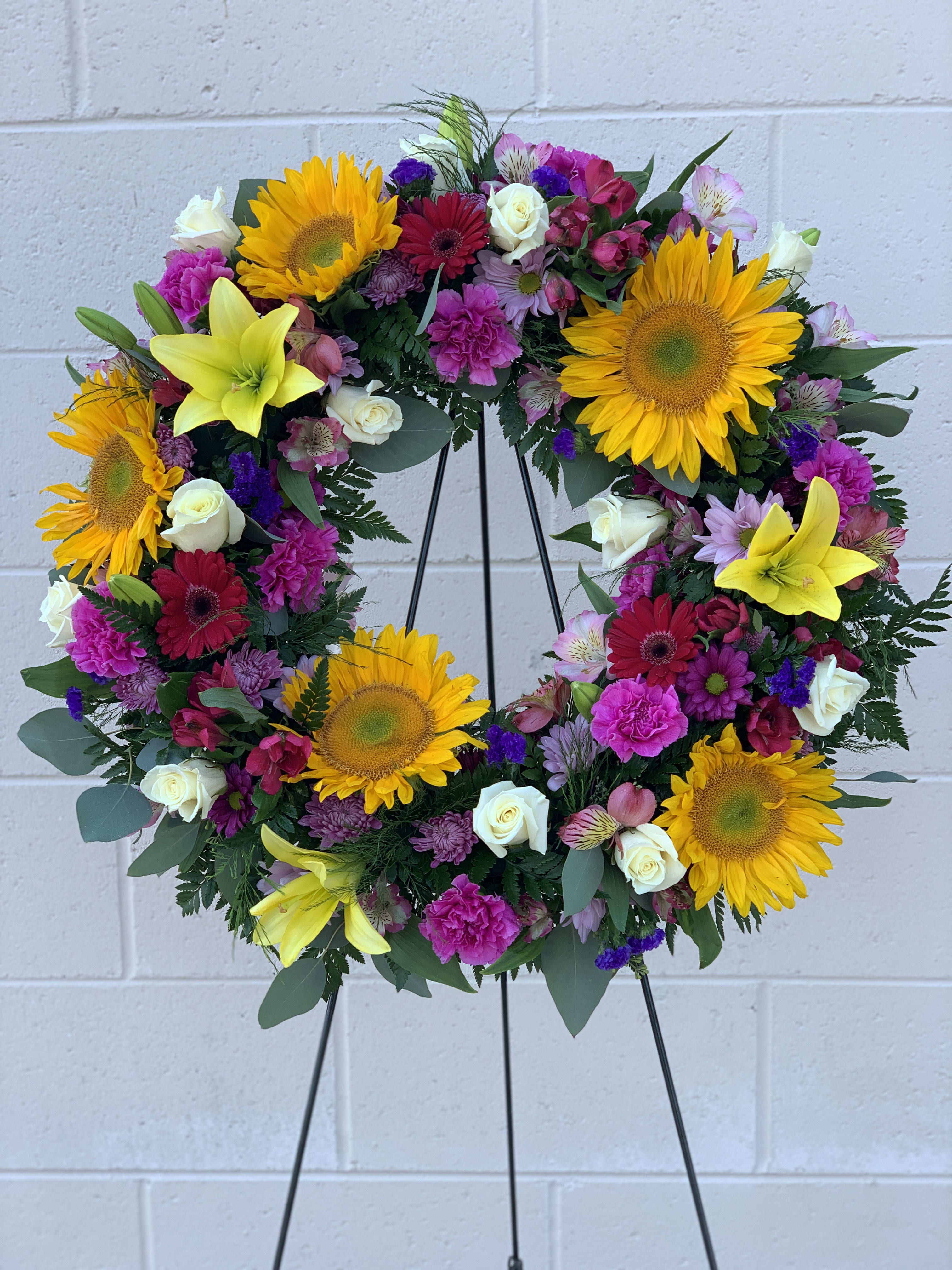 Colorful floral wreath with sunflowers, lilies, and roses on a black stand