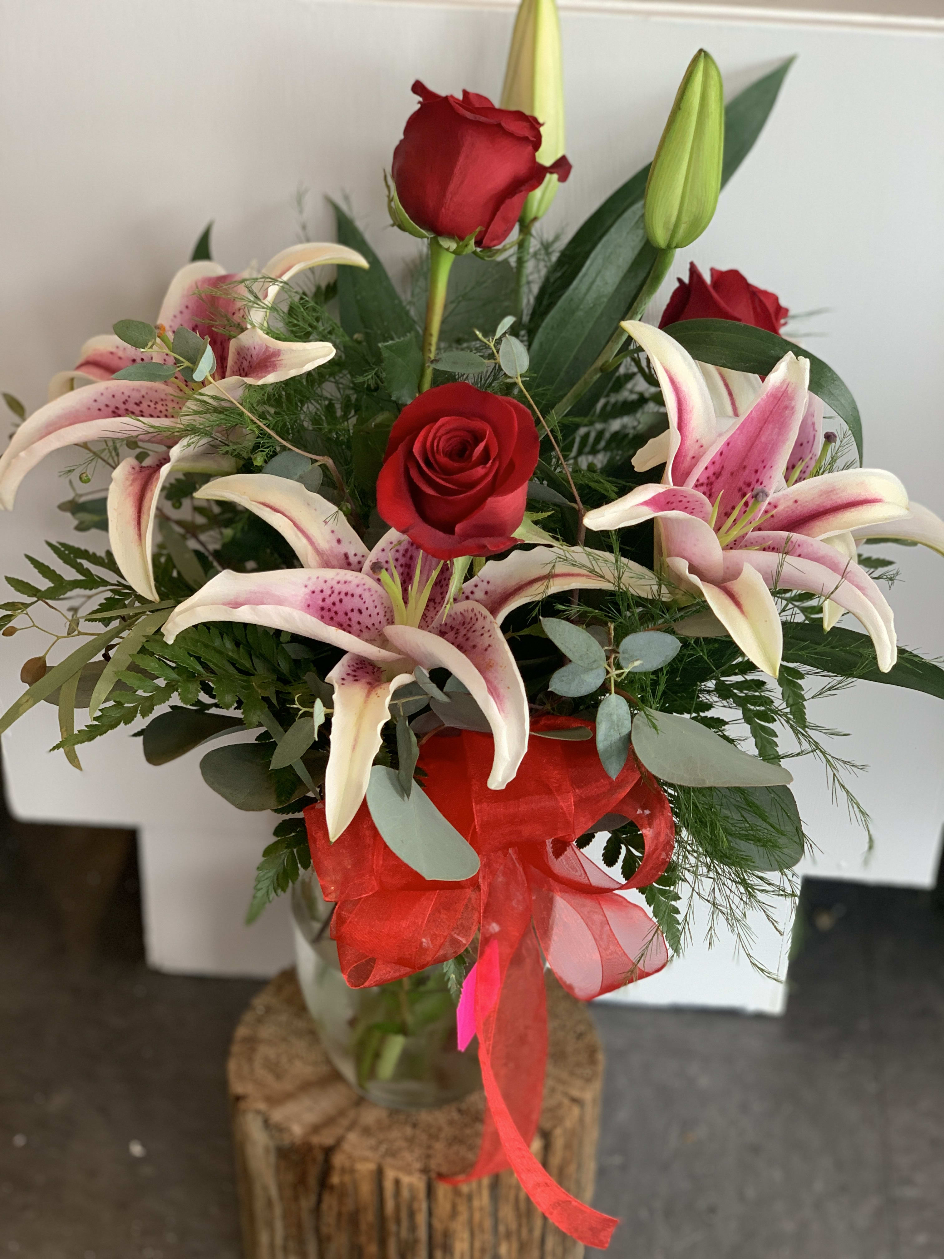 Arrangement of red roses and pink lilies in a clear glass vase with a red bow.
