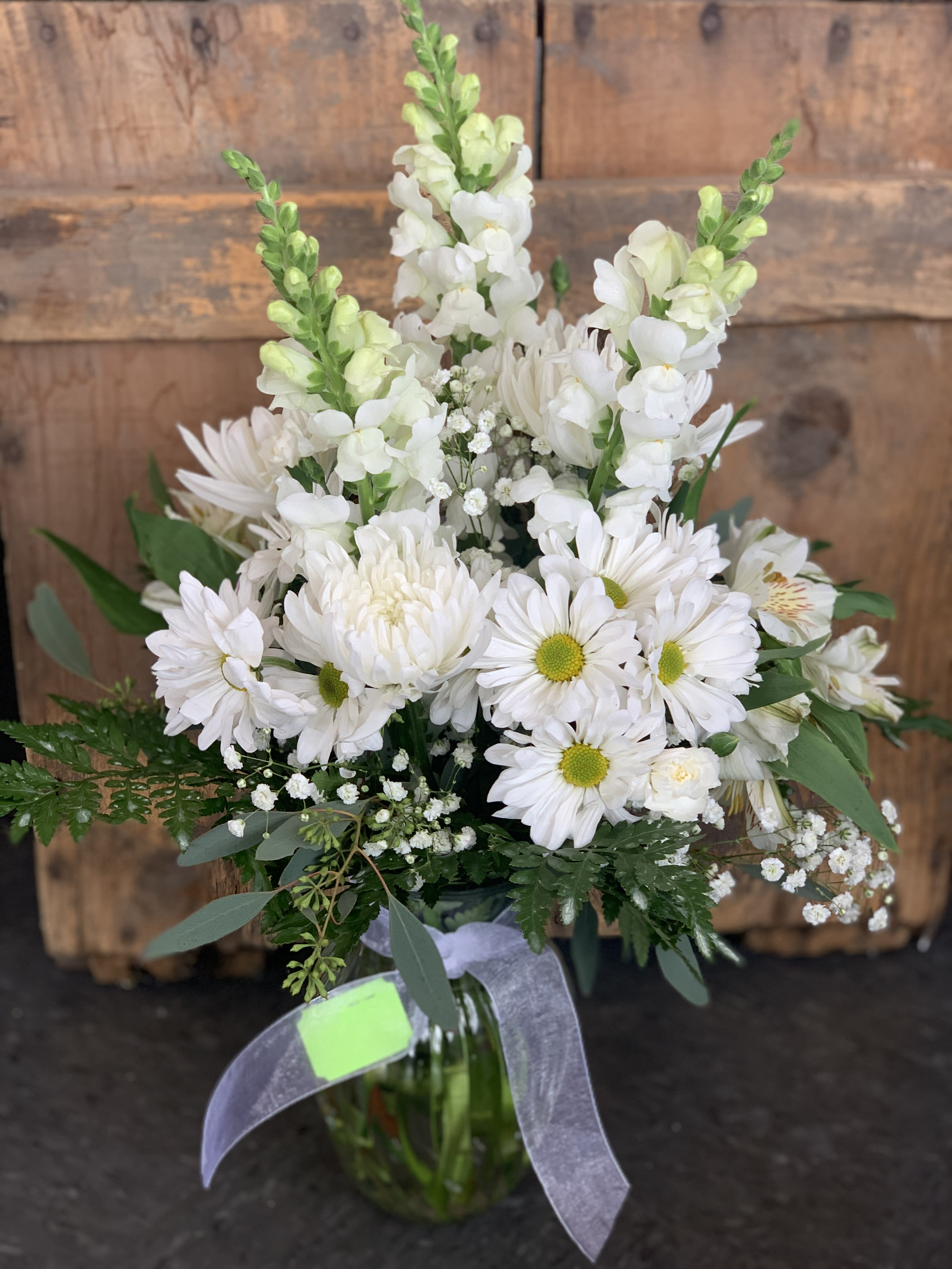 White daisies and snapdragons in a glass vase with greenery
