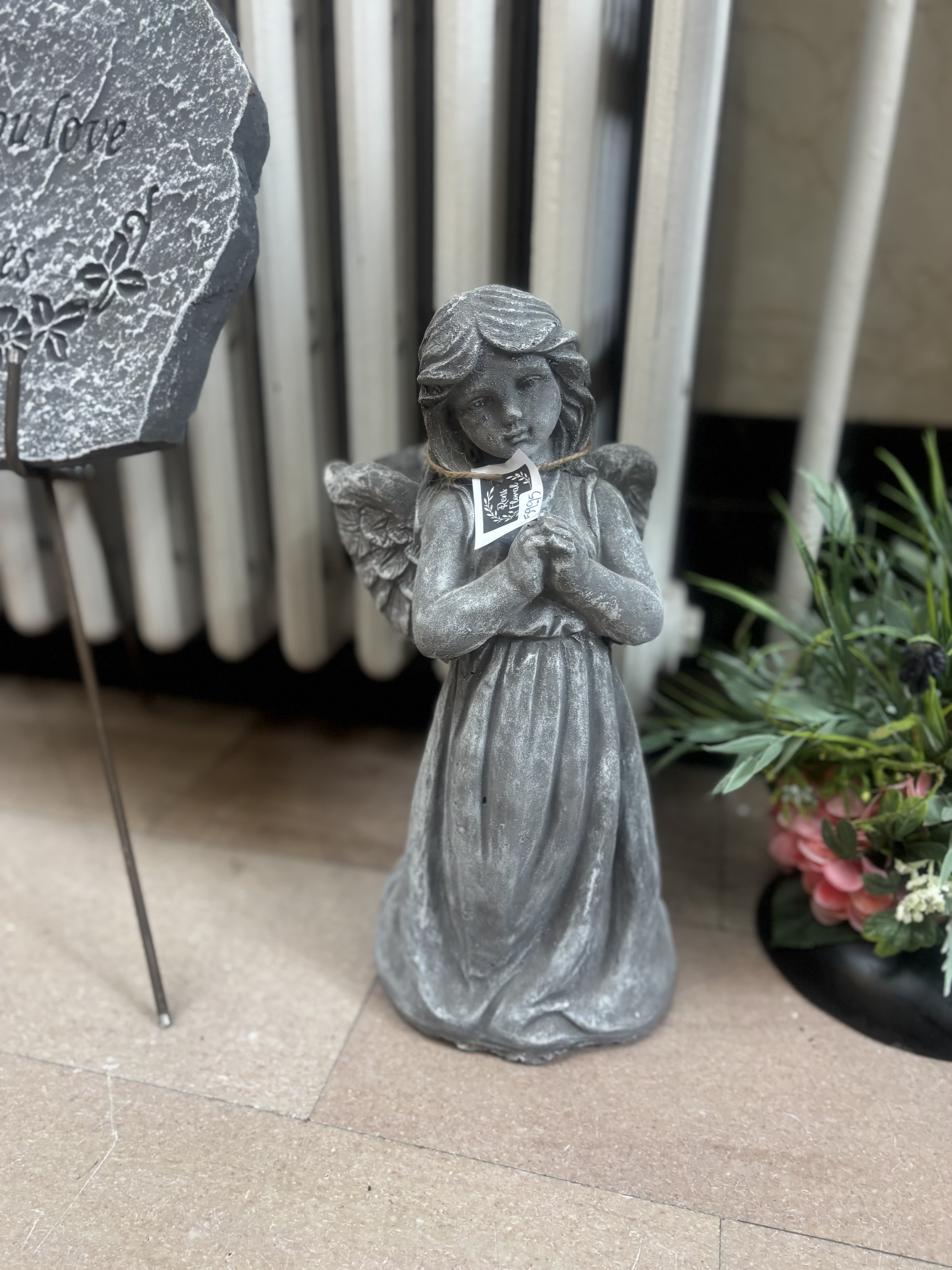 Gray angel statue with clasped hands beside a floral display