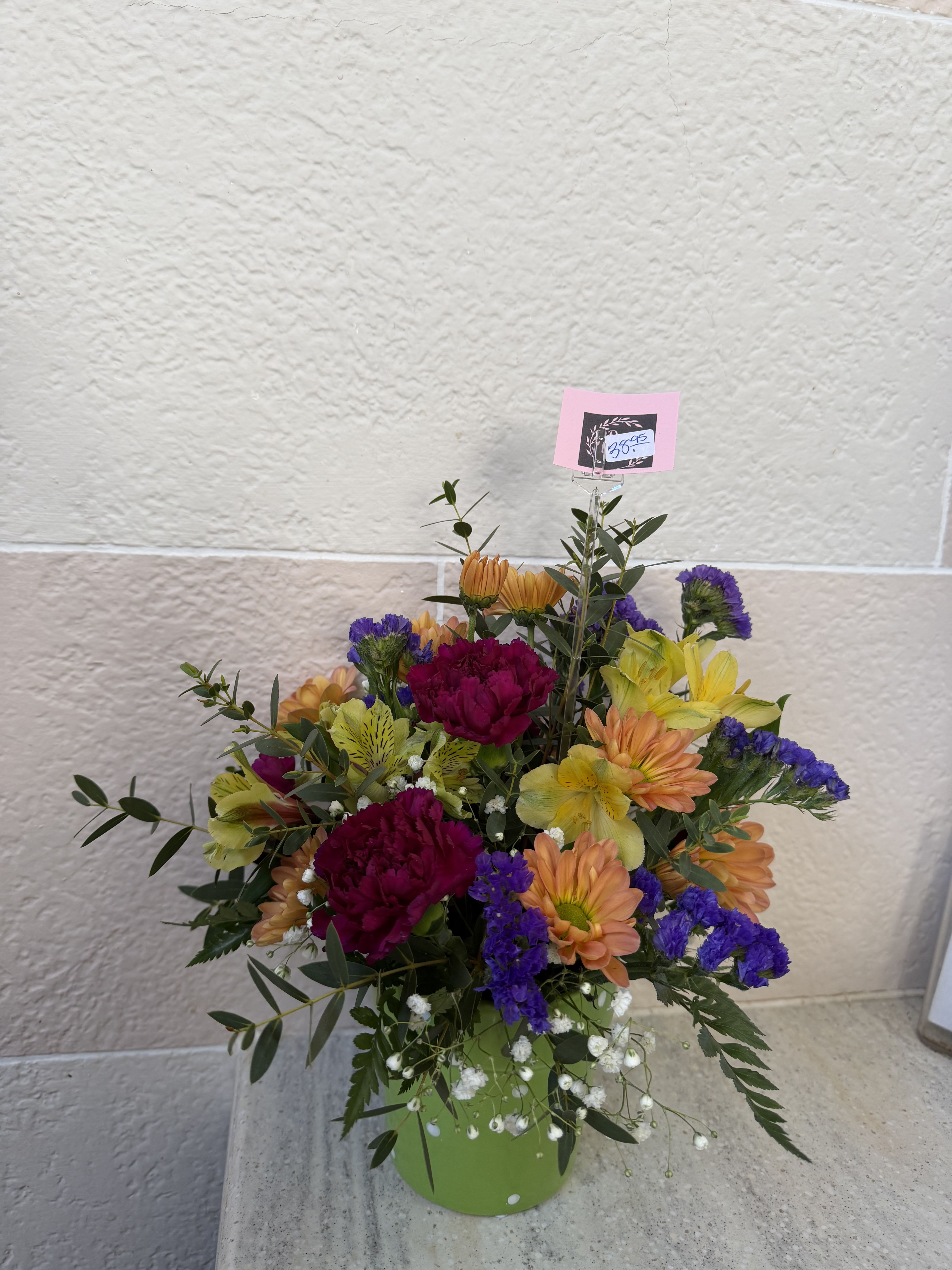 Mixed bouquet in a green container with orange, yellow, purple, and magenta flowers