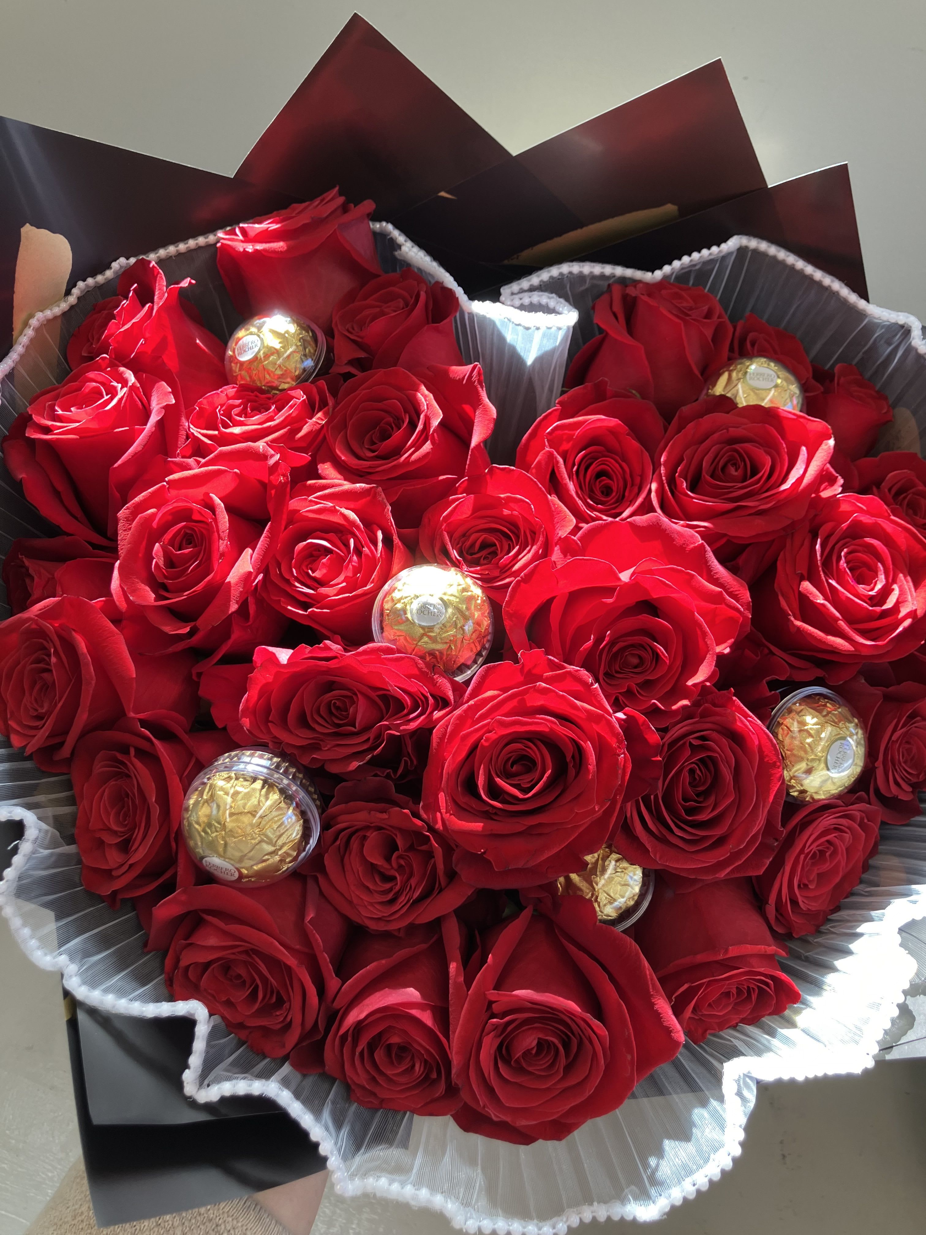 Ramos Style Wrapped Roses - Two dozen popular red roses tightly wrapped with white Korean pleated pearl fabric, sleek black wrap and 6 cololates.