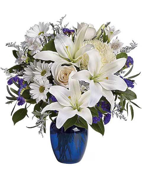 White lilies and daisies arranged in a blue glass vase