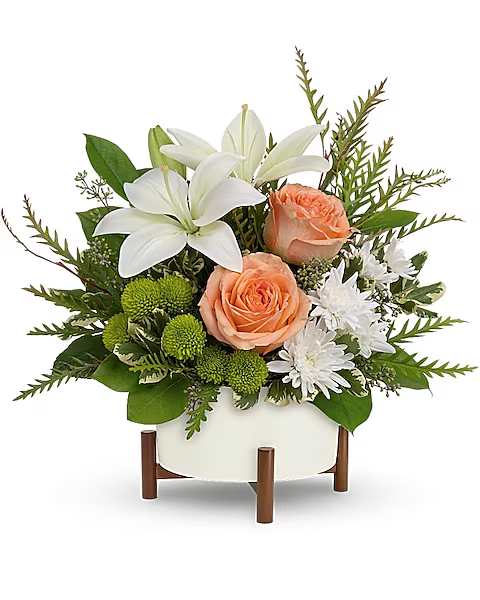White lilies and peach roses in a white container with green accents