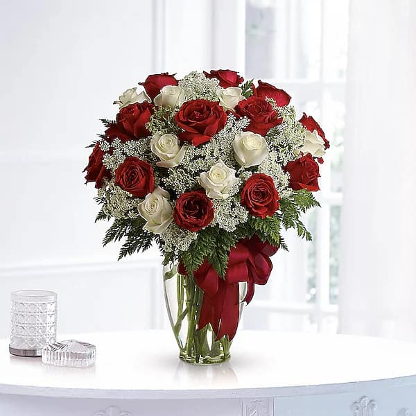 Red and white roses arranged in a clear glass vase with a red ribbon