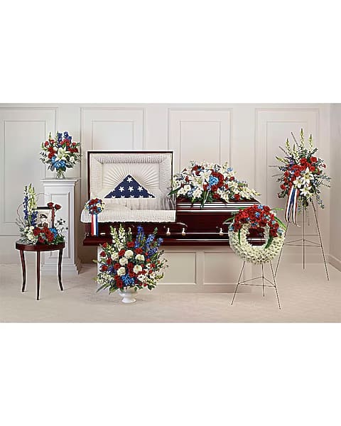 Funeral casket surrounded by red, white, and blue floral sprays