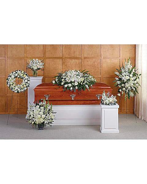 White funeral casket surrounded by white floral sprays and wreaths