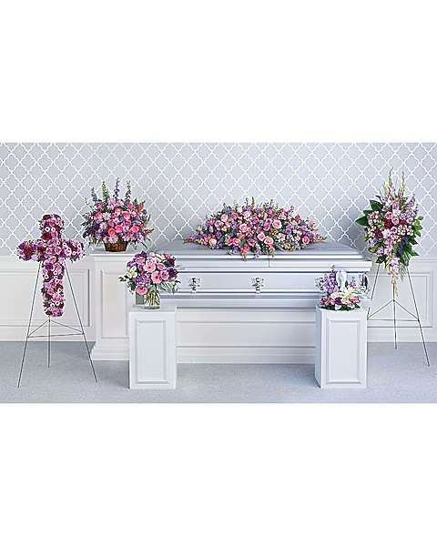 Floral funeral display with pink and purple arrangements around a white casket