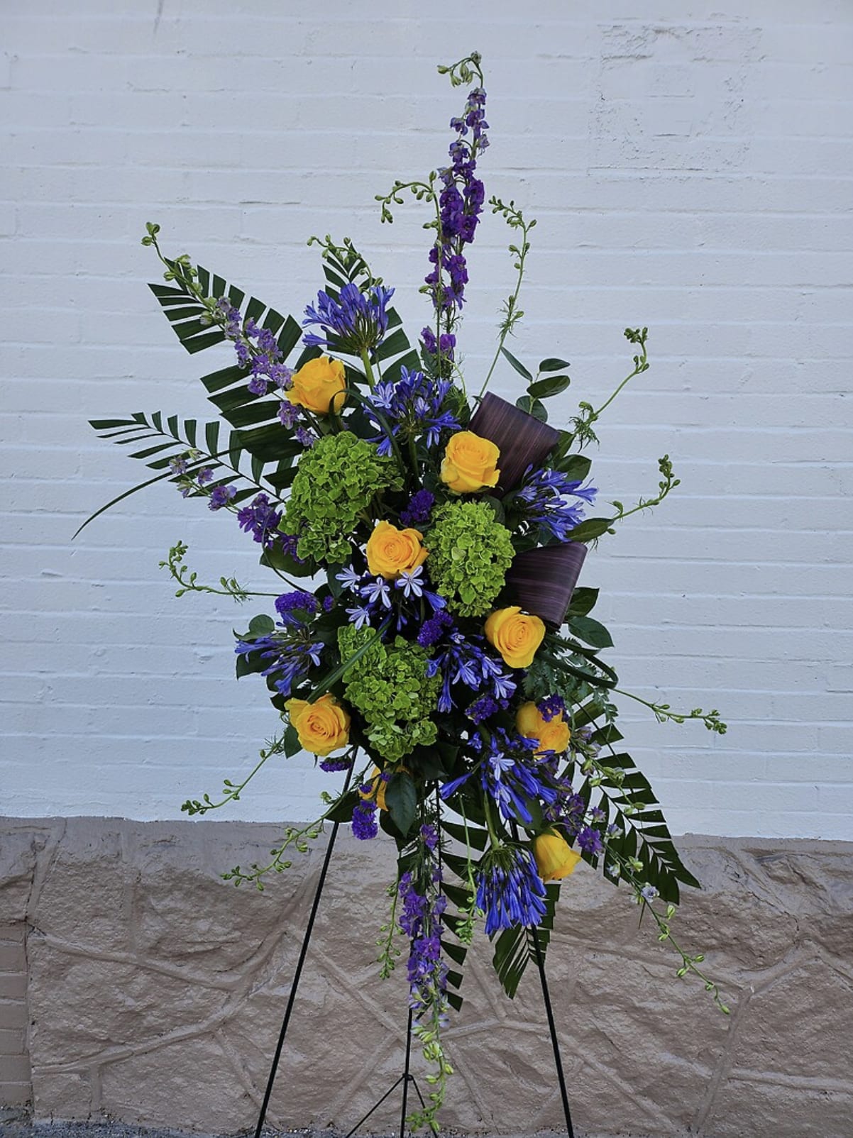 Tall floral spray with yellow roses, purple blooms, and green hydrangeas on a stand