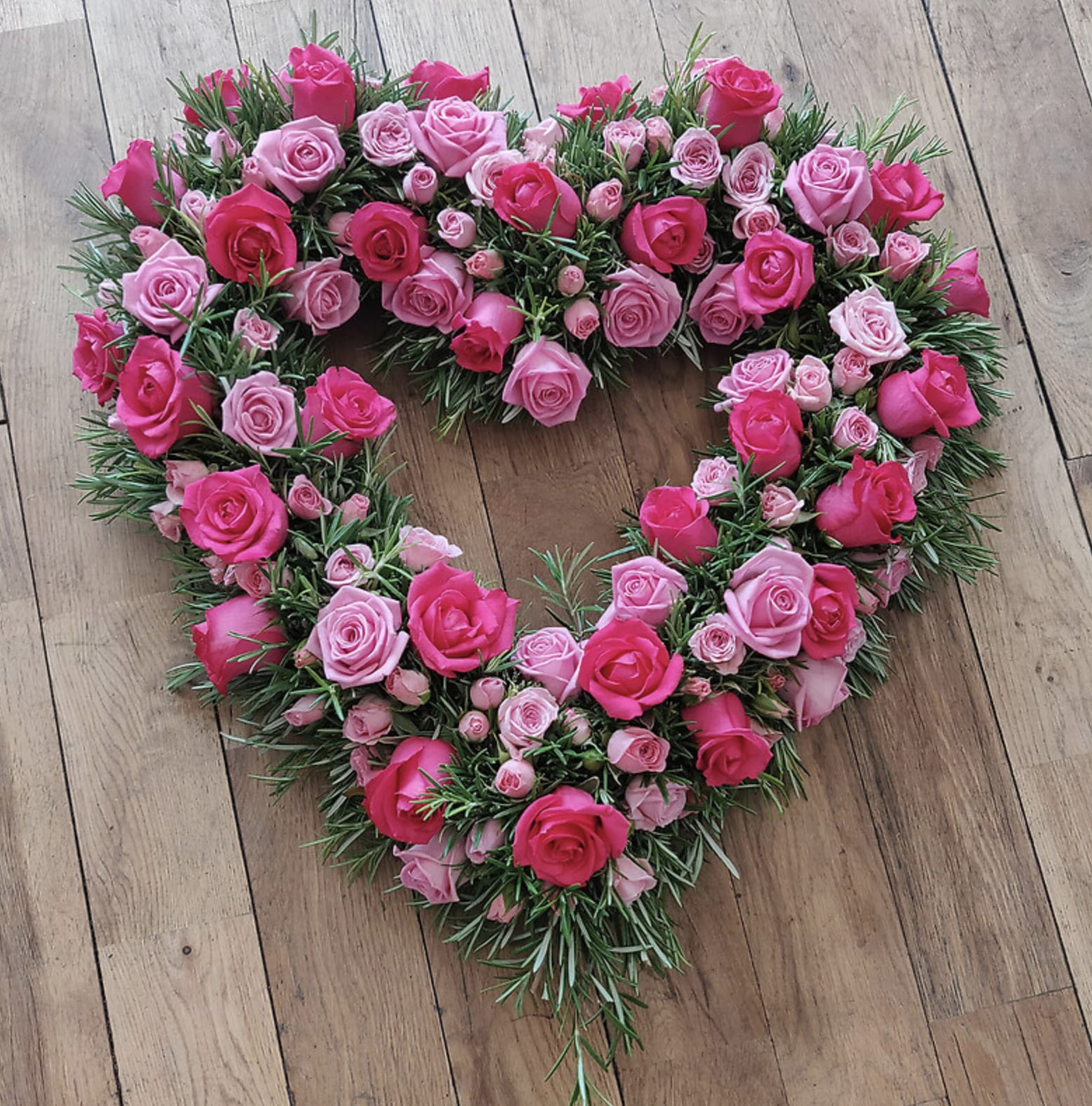 Heart-shaped rose arrangement in pink tones on a wooden floor