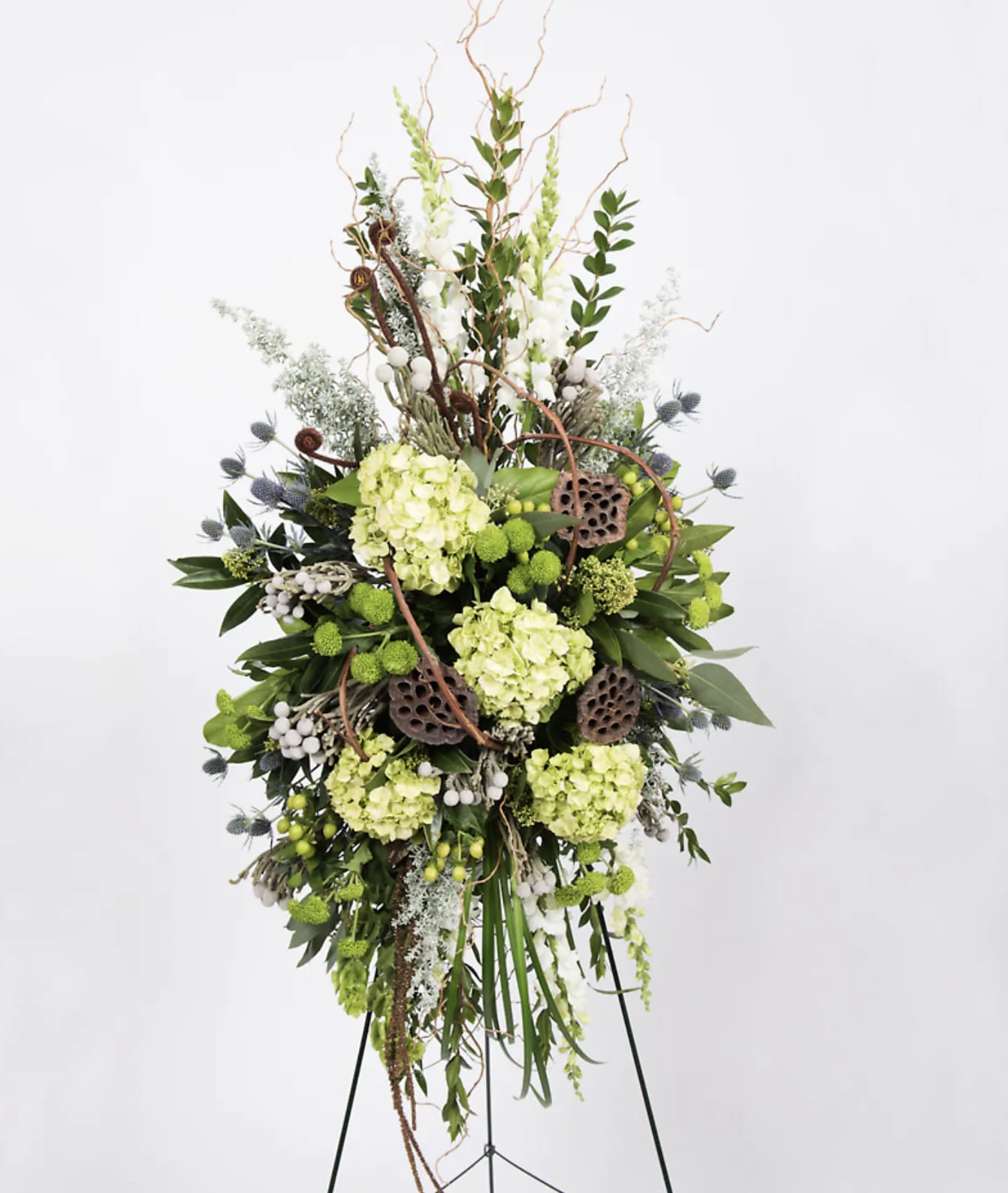 Tall floral standing spray with green hydrangeas and lotus pods
