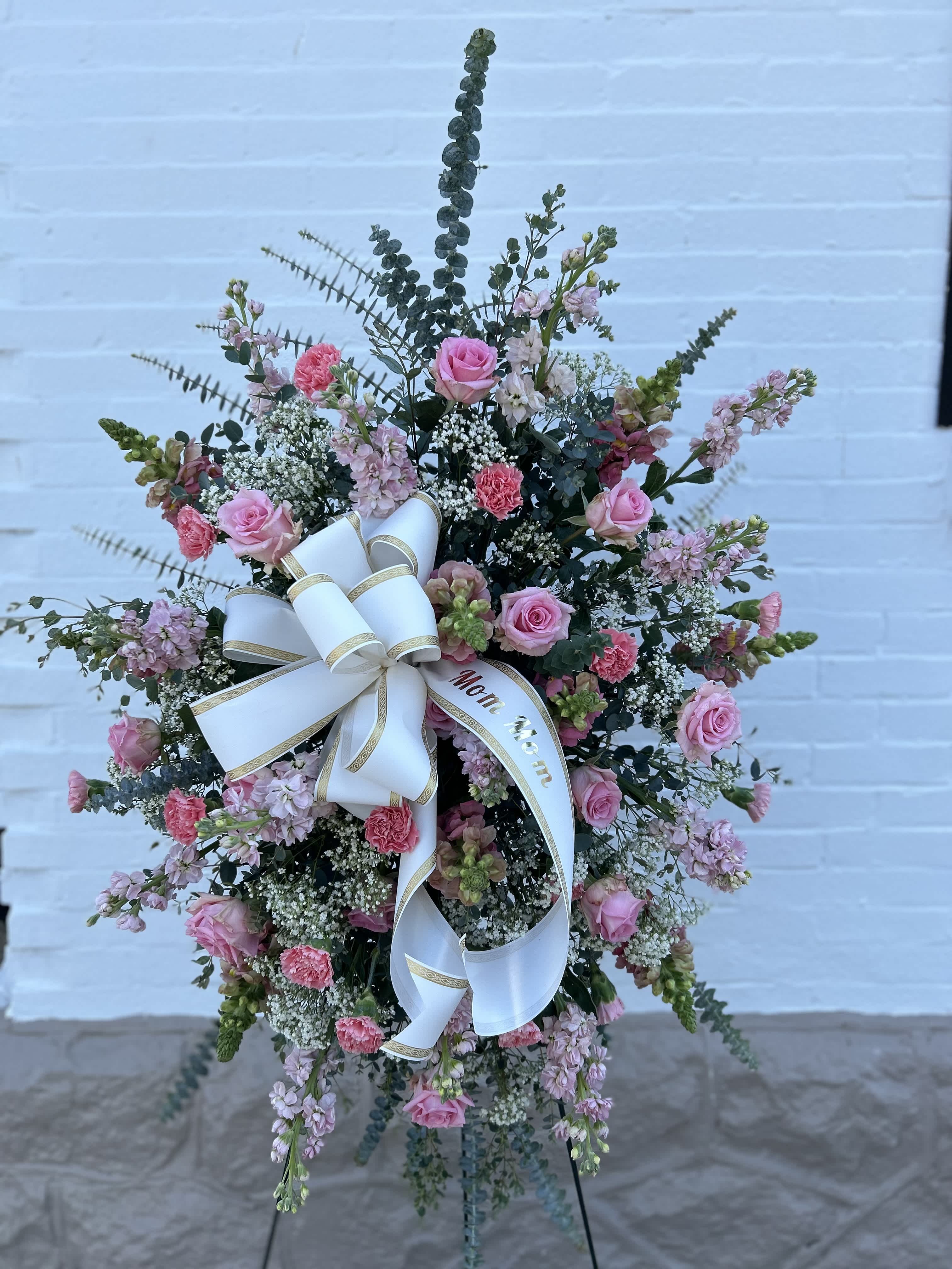 Standing floral spray with pink roses and carnations, finished with a white ribbon bow