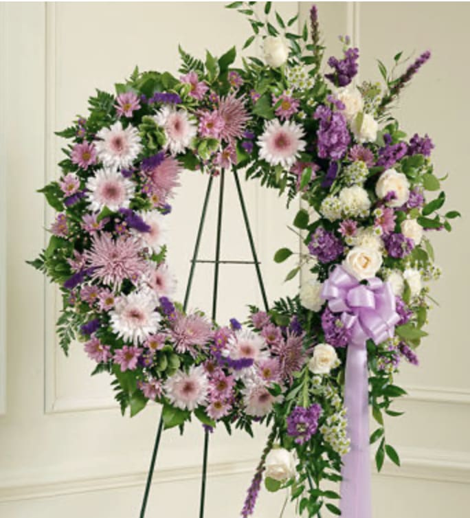 Purple and white floral wreath on a stand with a lavender ribbon